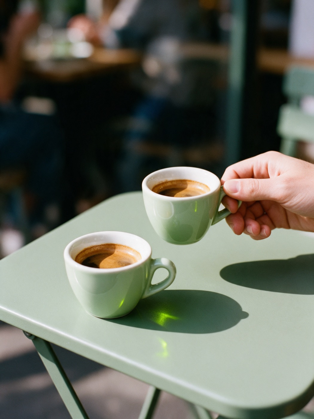 Duas xícaras de café expresso em uma mesa verde de café, uma sendo levantada